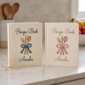 Personalized hand embroidered recipe book featuring fork, knife and spoon tied with a ribbon on a linen cover with custom name embroidery.