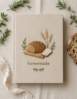 Hand embroidered recipe book featuring artisan bread loaf wheat stalks wooden board and farmhouse botanical accents on linen cover