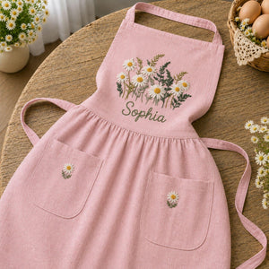 Personalized hand embroidered daisy flower apron featuring custom name embroidery, white daisies, and botanical greenery on natural linen fabric.