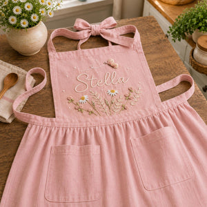 Personalized hand embroidered linen apron featuring wildflowers, daisies, botanical foliage, butterfly embroidery, and custom name embroidery on green linen fabric.