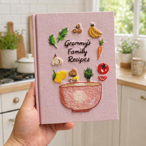 Personalized hand embroidered recipe book featuring fresh vegetables herbs garlic mushrooms lemons tomatoes and a rustic mixing bowl design on a linen cover.