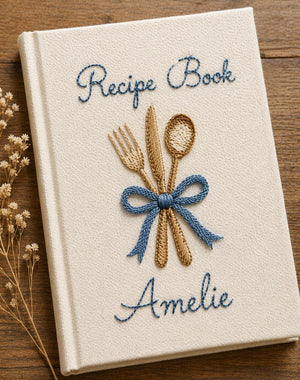 Personalized hand embroidered recipe book featuring fork, knife and spoon tied with a ribbon on a linen cover with custom name embroidery.
