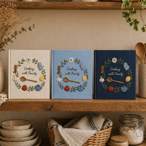 Personalized hand embroidered recipe book featuring cooking spoon, garlic, lemon, tomato, oven mitt, cooking pot, herbs and family kitchen themed embroidery on blue linen cover.