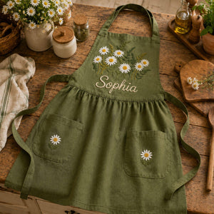 Personalized hand embroidered daisy flower apron featuring custom name embroidery, white daisies, and botanical greenery on natural linen fabric.