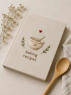Hand embroidered recipe book featuring mixing bowl whisk heart and botanical accents on linen hardcover cover