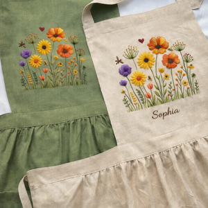 Personalized hand embroidered linen apron featuring colorful wildflowers, meadow flowers, botanical embroidery, and custom name embroidery on green linen fabric.