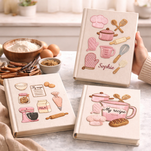 Personalized hand embroidered recipe book featuring pink baking tools, stand mixer, oven mitts, recipe cards, measuring cups, chef hat, whisk, and bakery-inspired embroidery on linen cover.