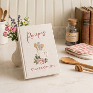 Hand embroidered recipe book featuring a vintage utensil pitcher with pink roses and personalized name on a linen cover.