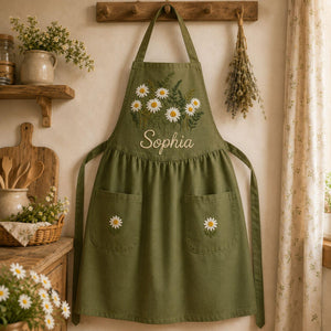 Personalized hand embroidered daisy flower apron featuring custom name embroidery, white daisies, and botanical greenery on natural linen fabric.