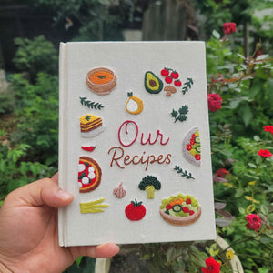 Hand embroidered recipe book featuring vegetables salads pizza lasagna soups herbs and family meal inspired food illustrations on linen cover