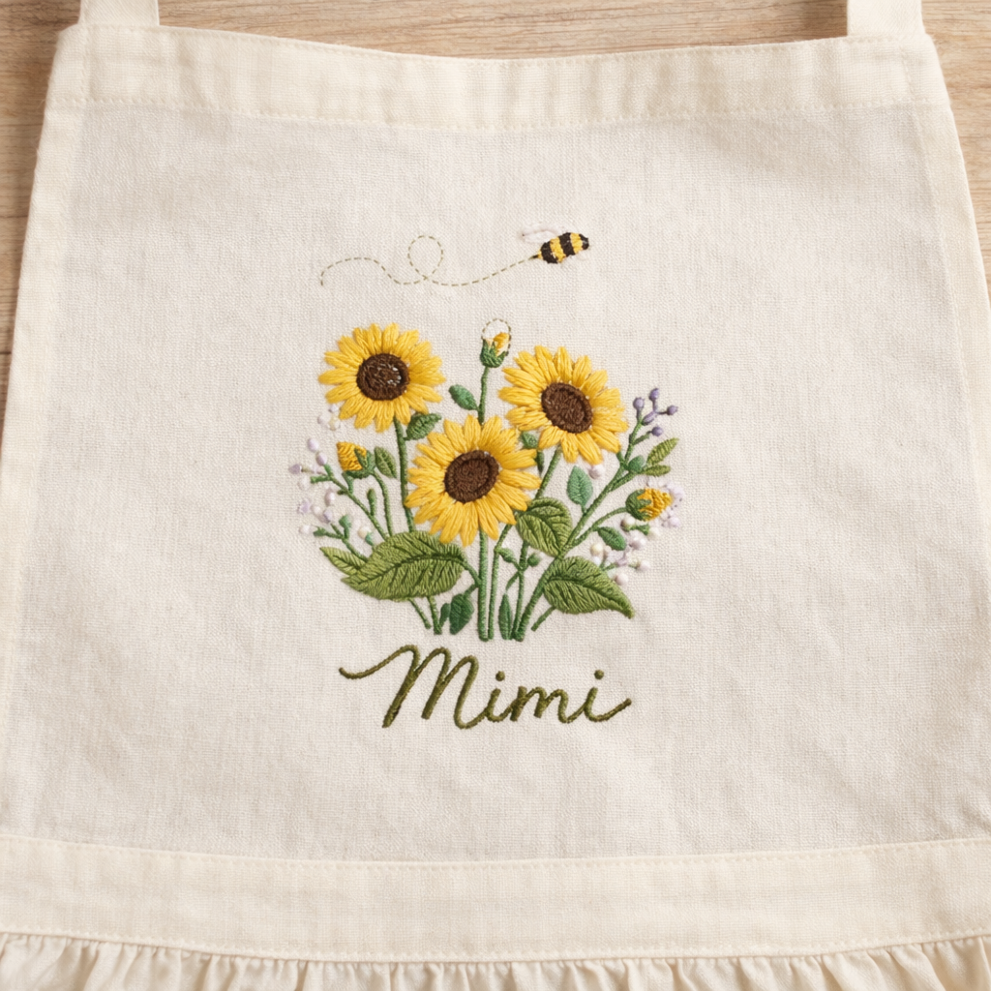 Personalized hand embroidered linen apron featuring sunflowers, wildflowers, honey bee embroidery, and custom name personalization.