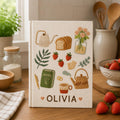 Personalized hand embroidered recipe book featuring cottage kitchen motifs, strawberries, teapot, herbs, lemons, avocado, olive oil and fresh cooking ingredients on linen cover.