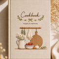 Hand embroidered farmhouse cookbook featuring rustic kitchen shelf daisies tomatoes herbs garlic and wooden cutting board on linen cover
