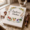 Personalized hand embroidered recipe book featuring sunflowers, strawberries, carrots, broccoli, baking tools and cottage garden floral wreath design on linen cover.