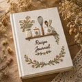 Hand embroidered recipe journal featuring floral kitchen shelf with vintage jars whisk baking utensils and botanical wreath on linen cover