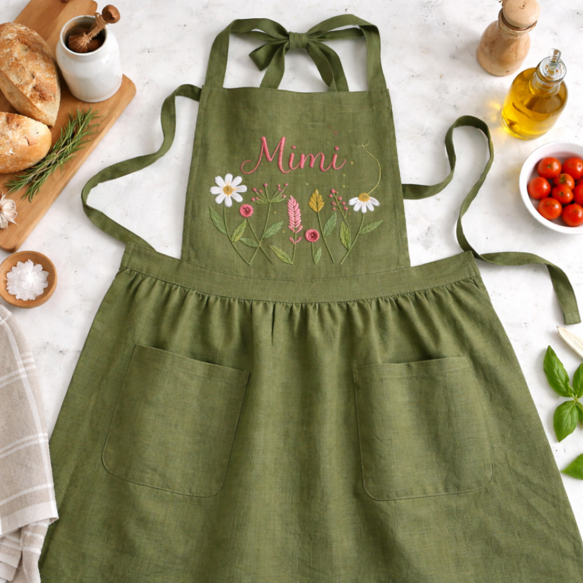 Personalized hand embroidered wildflower linen apron featuring custom name embroidery and delicate meadow flower design on a sage green apron.