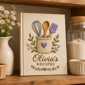 Personalized hand embroidered recipe book featuring rustic utensil holder, whisk, wooden spoon, spatula, daisies, greenery, and cottage kitchen design on linen cover.