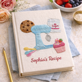 Personalized hand embroidered recipe book featuring a vintage stand mixer, cupcake, cookie, sugar bag and baking utensils on a linen cover.