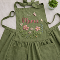 Personalized hand embroidered cottage garden apron featuring custom name, floral embroidery, butterflies, and botanical details on green linen fabric.