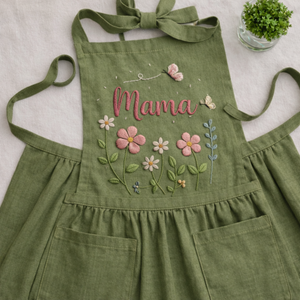 Personalized hand embroidered cottage garden apron featuring custom name, floral embroidery, butterflies, and botanical details on green linen fabric.
