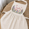 Personalized hand embroidered linen apron featuring colorful wildflowers, butterflies, lavender blooms, and custom name embroidery.
