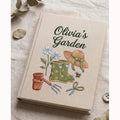 Personalized hand embroidered garden journal featuring rain boots flowers gardening tools and straw hat on linen cover