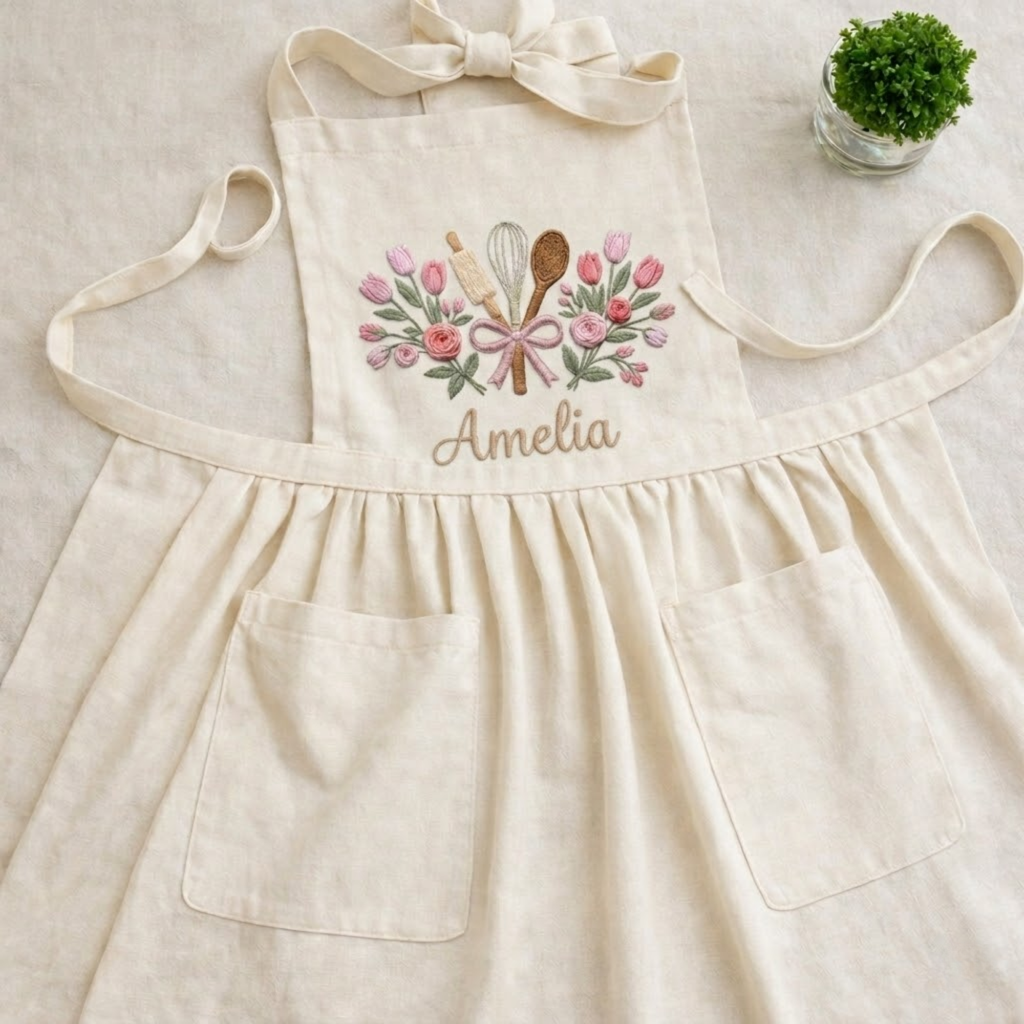 Personalized hand embroidered linen baker apron featuring floral baking utensils embroidery and custom name personalization on a natural beige apron.