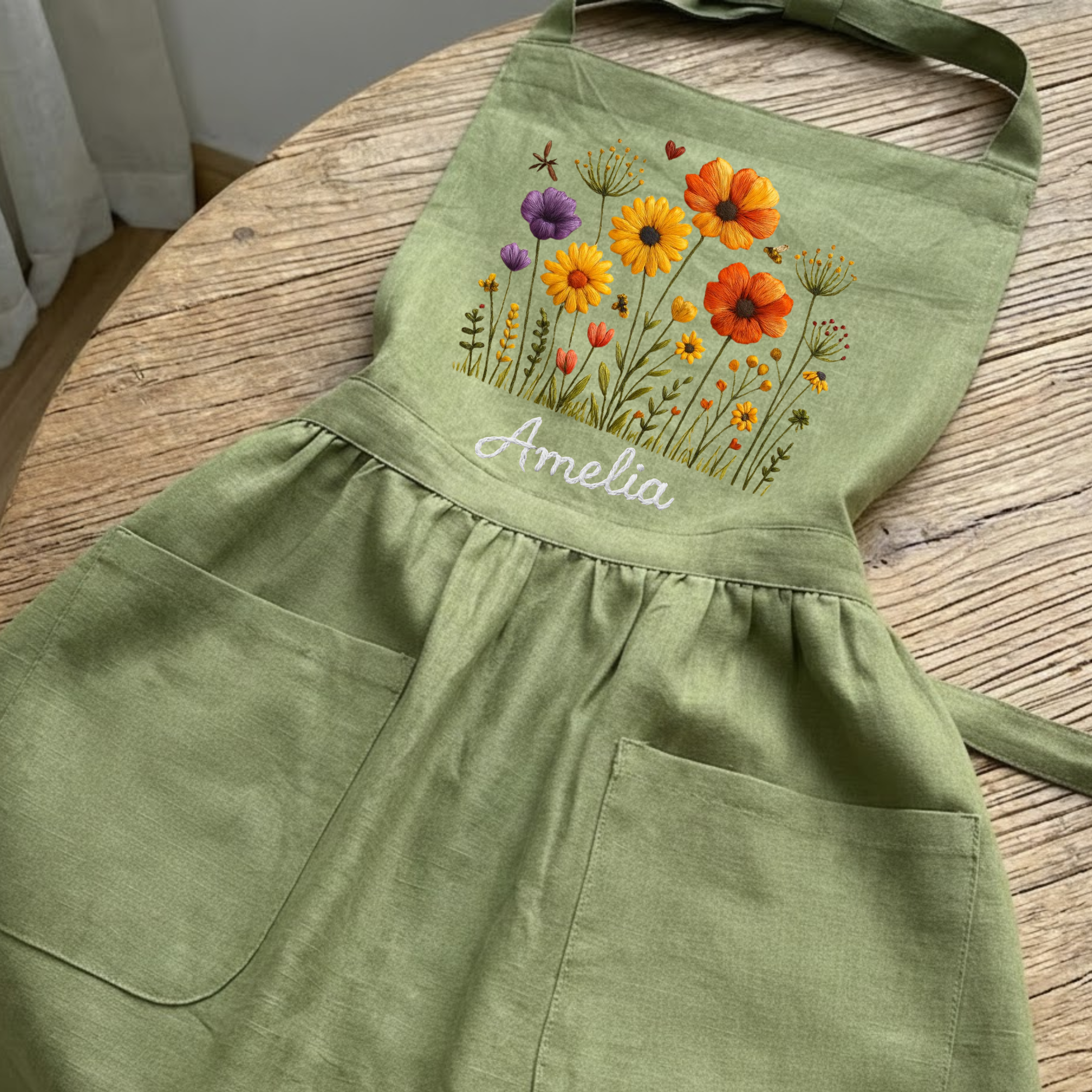 Personalized hand embroidered linen apron featuring colorful wildflowers, meadow flowers, botanical embroidery, and custom name embroidery on green linen fabric.