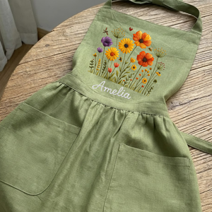 Personalized hand embroidered linen apron featuring colorful wildflowers, meadow flowers, botanical embroidery, and custom name embroidery on green linen fabric.
