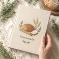 Hand embroidered recipe book featuring artisan bread loaf wheat stalks wooden board and farmhouse botanical accents on linen cover