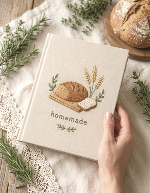 Hand embroidered recipe book featuring artisan bread loaf wheat stalks wooden board and farmhouse botanical accents on linen cover