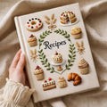 Hand embroidered recipe book featuring cakes, cupcakes, donuts, croissants and botanical wreath design on a linen cover.