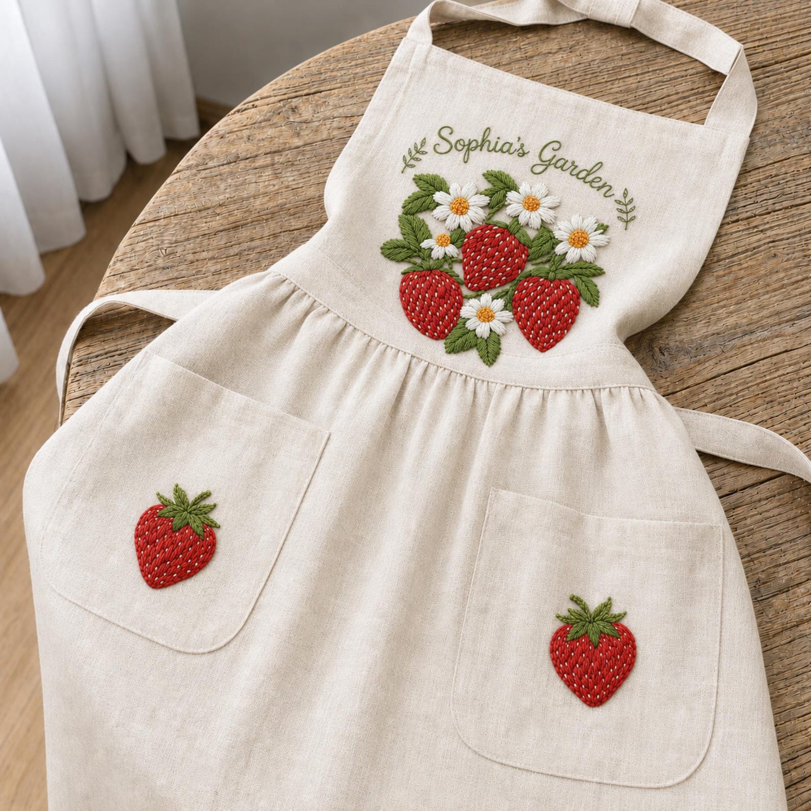 Personalized hand embroidered linen apron featuring strawberries, daisy flowers, botanical garden embroidery, and custom name personalization.
