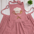 Personalized baker hand embroidered linen apron featuring chef hat, whisk, wooden spoon, and custom name embroidery, baking apron gift for bakers and home cooks.