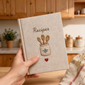 Hand embroidered recipe book featuring rustic utensil holder with wooden spoons and farmhouse kitchen embroidery on linen cover