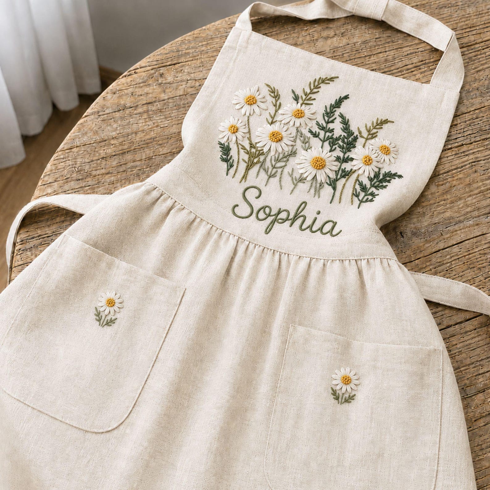Personalized hand embroidered daisy flower apron featuring custom name embroidery, white daisies, and botanical greenery on natural linen fabric.