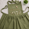 Personalized hand embroidered linen apron featuring wildflowers, daisy flowers, botanical foliage, butterfly embroidery, and custom name personalization on green linen fabric.