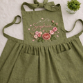 Personalized hand embroidered linen apron featuring pink rose floral embroidery and custom name personalization on a sage green apron.
