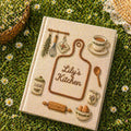 Hand embroidered recipe book featuring personalized cutting board design with rolling pin, whisk, sugar jar, teacup, eggs and cottage kitchen accents.