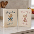 Personalized hand embroidered recipe book featuring fork, knife and spoon tied with a ribbon on a linen cover with custom name embroidery.
