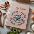 Personalized hand embroidered recipe book featuring floral baking wreath with mixing bowl whisk rolling pin and baking ingredients on linen cover