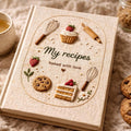 Hand embroidered recipe book featuring strawberries, cupcakes, cakes, cookies, whisks and baking tools on a linen cover.