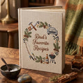Personalized hand embroidered recipe book featuring fishing rod, barbecue grill, vintage truck, woodworking tools, pine branches and outdoor dad themed design on linen cover.