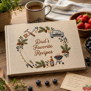 Personalized hand embroidered recipe book featuring fishing rod, barbecue grill, vintage truck, woodworking tools, pine branches and outdoor dad themed design on linen cover.