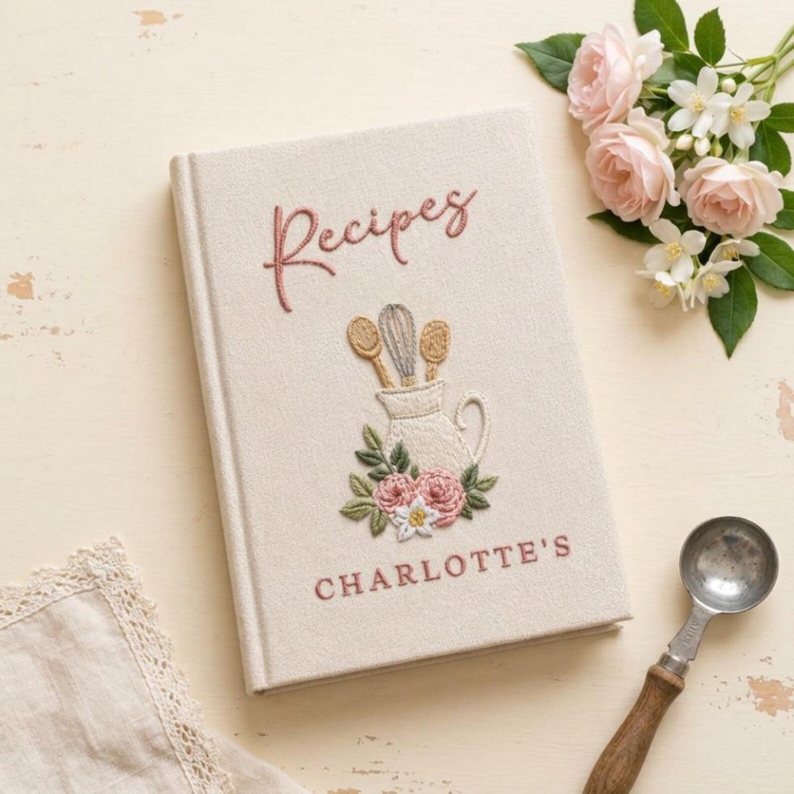 Hand embroidered recipe book featuring a vintage utensil pitcher with pink roses and personalized name on a linen cover.