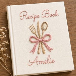 Personalized hand embroidered recipe book featuring fork, knife and spoon tied with a ribbon on a linen cover with custom name embroidery.