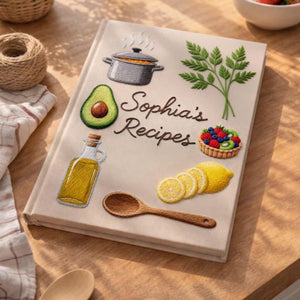 Personalized hand embroidered recipe book featuring cottage kitchen motifs, strawberries, teapot, herbs, lemons, avocado, olive oil and fresh cooking ingredients on linen cover.