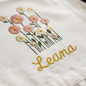 Personalized hand embroidered wildflower bouquet linen apron featuring pastel pink flowers and custom name embroidery, cottagecore floral kitchen apron gift.