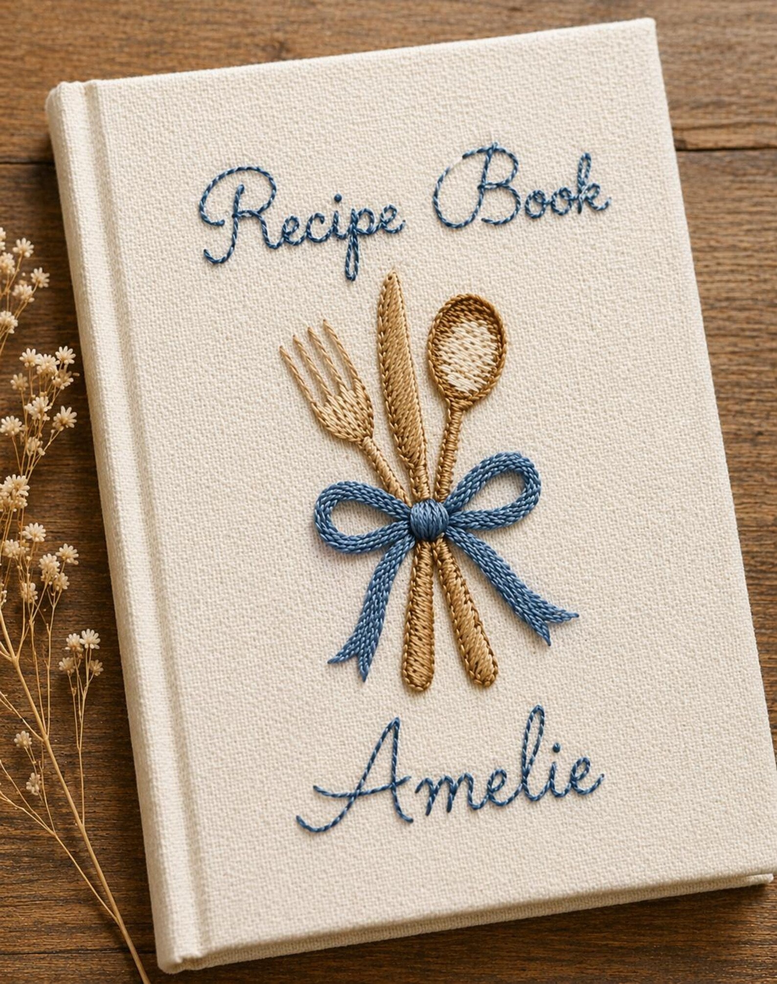 Personalized hand embroidered recipe book featuring fork, knife and spoon tied with a ribbon on a linen cover with custom name embroidery.