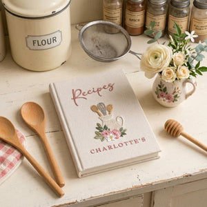 Hand embroidered recipe book featuring a vintage utensil pitcher with pink roses and personalized name on a linen cover.